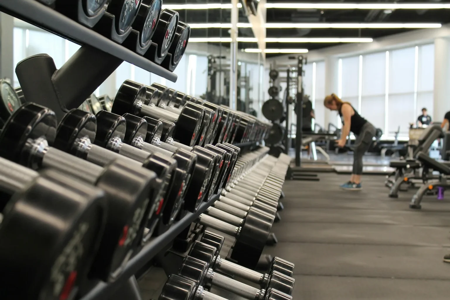 Gym Funding 7 Rows of dumbbells on a rack with members training in a busy gym