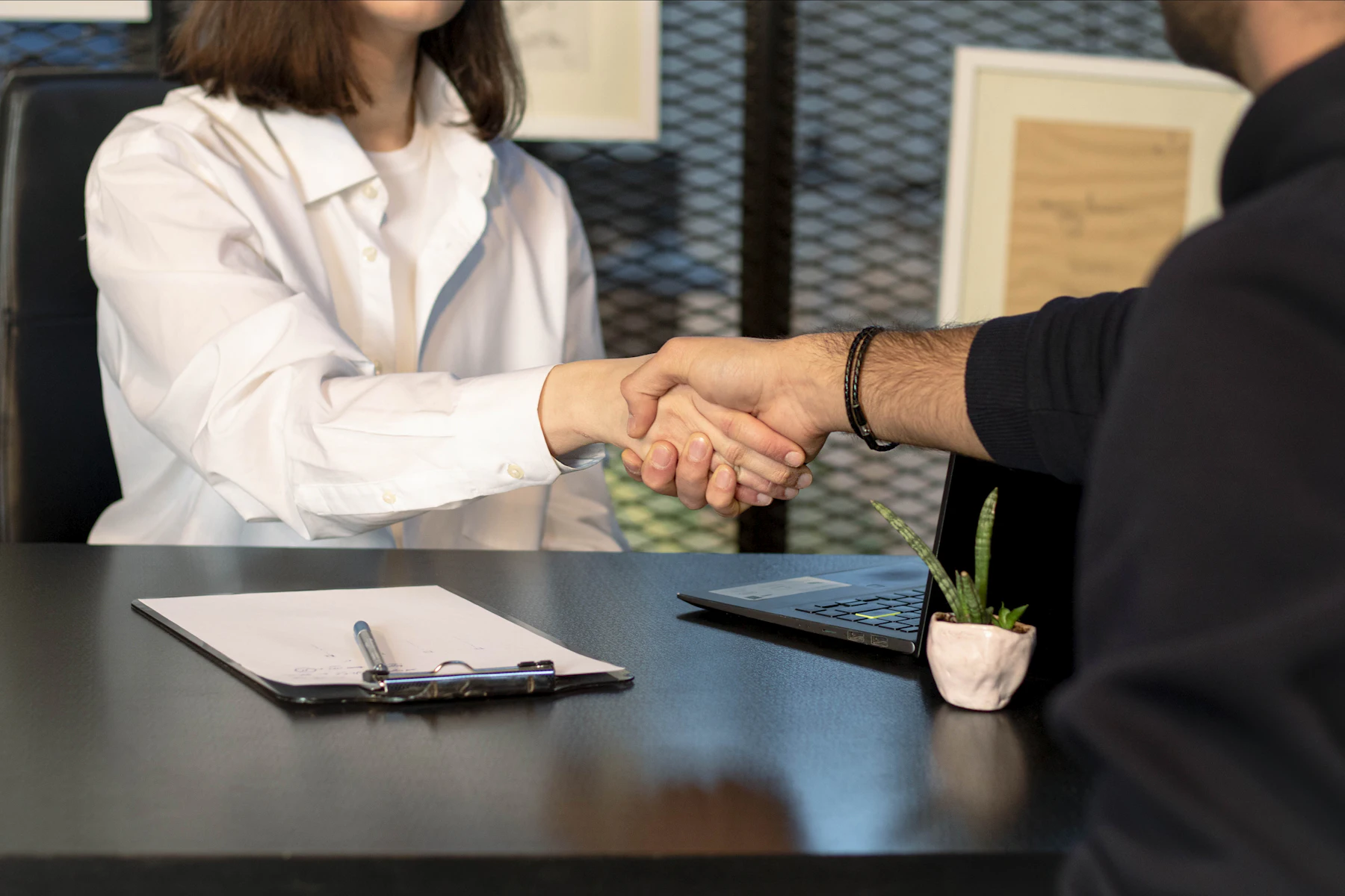 Man and woman shaking hands in front of a laptop