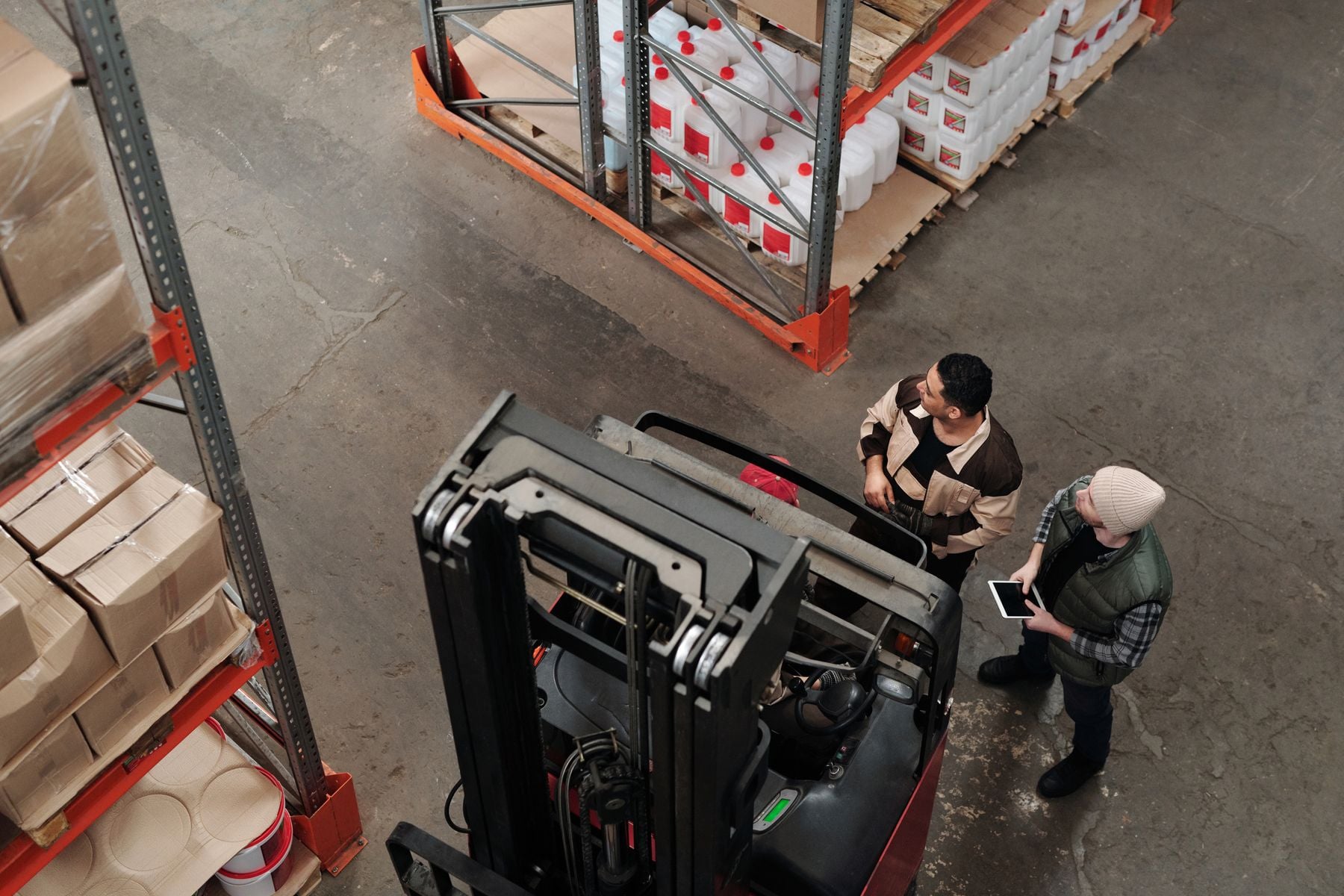 How Does Equipment Financing Work? Step by Step 2 Warehouse workers discussing logistics beside a forklift