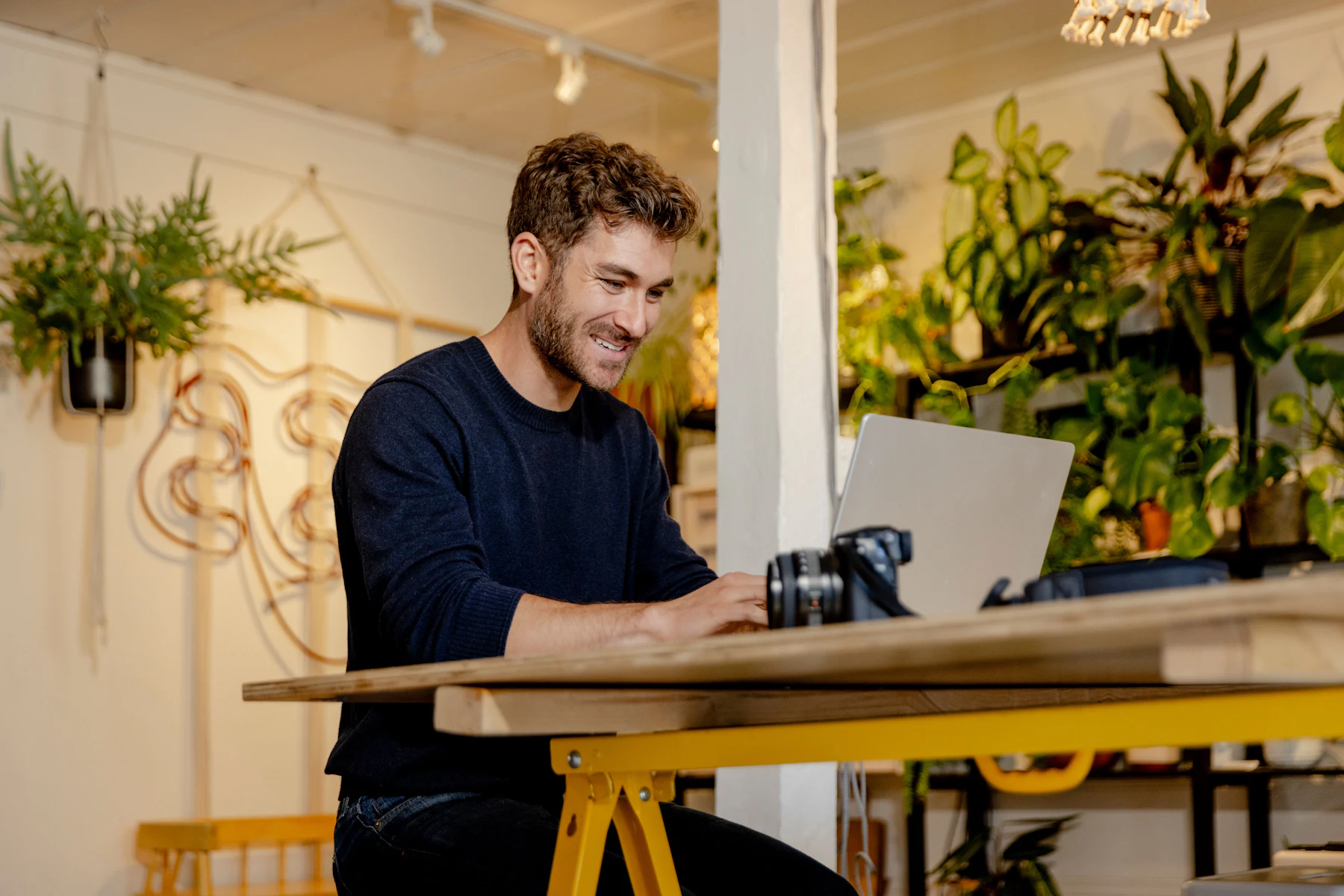 How to Get a Business Loan in 7 Steps (2026) 2 Business owner working on a laptop at a workbench surrounded by plants