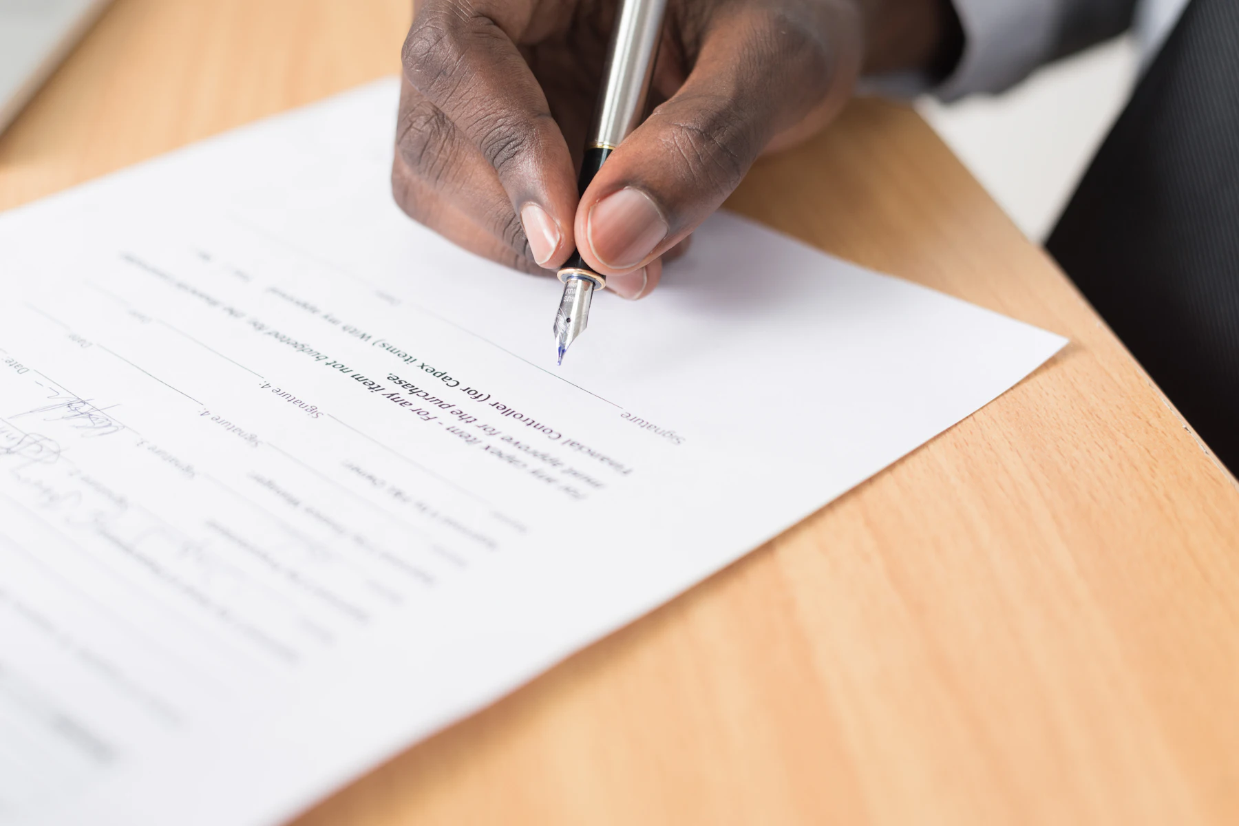 Hand signing a document on a wooden desk