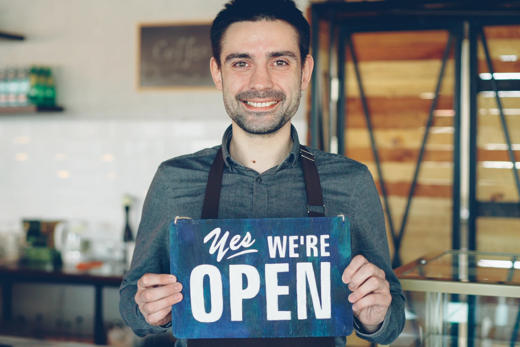 Los 5 Mejores Préstamos Rápidos para Negocios de Octubre 2026 2 Dueño de una cafetería sosteniendo un letrero de abierto
