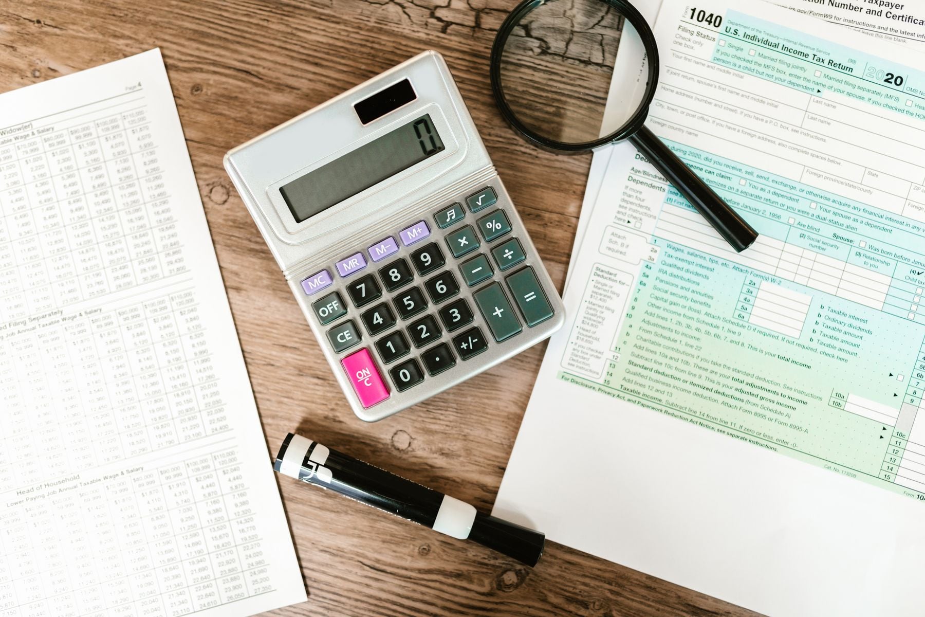 Tax forms, calculator and magnifying glass on a desk